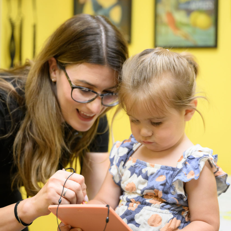 a woman helping a young girl read on a tablet