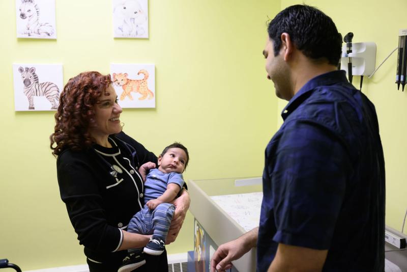 a woman holding a baby while talking to a man