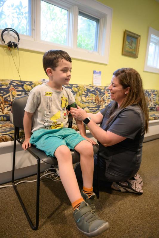 a boy sitting in a chair while a medical provider wraps a blood pressure cuff around his arm