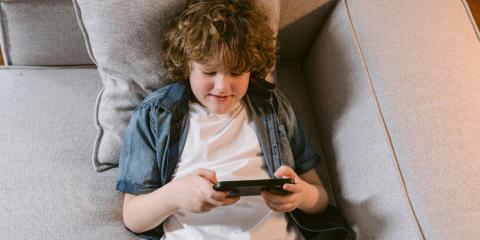 a boy lying on a couch playing with a phone