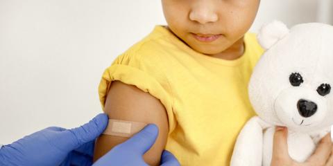 a child holding a teddy bear getting a bandaid placed on their arm