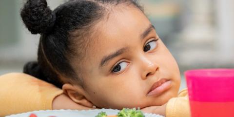 a child looking sorrowfully at a plate of vegetables